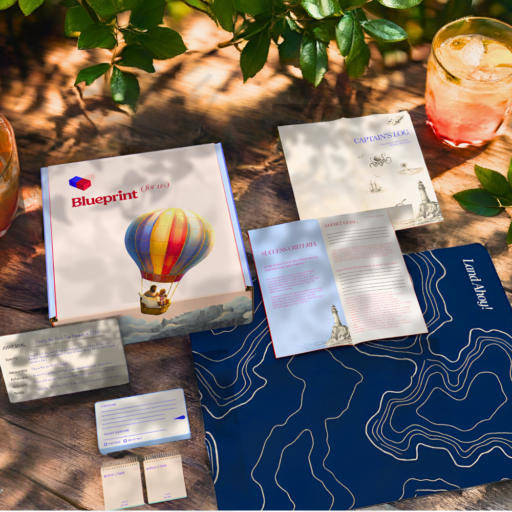 Collection of promotional materials including a book titled 'Blueprint' with a hot air balloon illustration, on a wooden surface with a natural background.